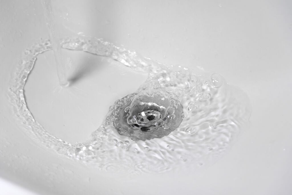 Close-up Of A Stream Of Clean Water Flowing Into A Clean White C Close-up of water swirling and draining smoothly in a clean white sink, indicating a clear and unclogged drain line after professional plumbing service.
